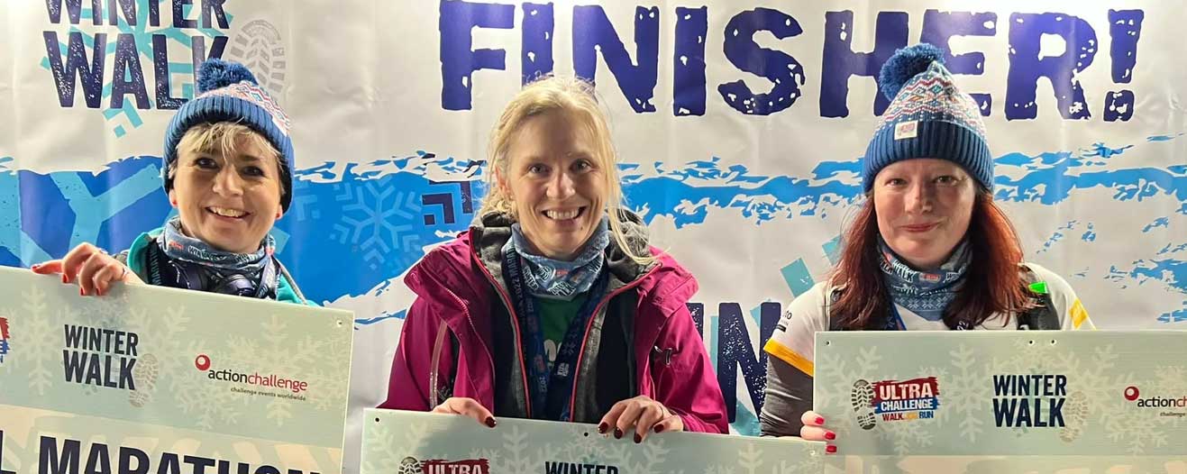Three female event finishers holding up cards showing how far they walked in the London Winter Walk.
