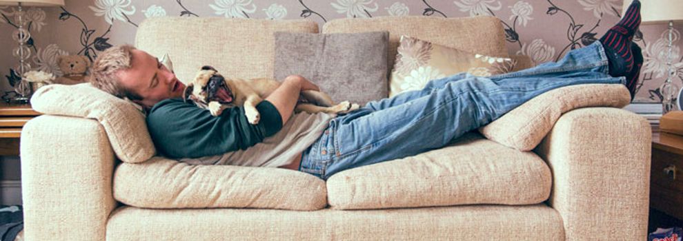 Man laying on the sofa with a dog yawning in his arms